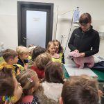 Grupa dzieci w wieku przedszkolnym otrzymuje lekcję weterynarii, którą nauczyciel wyjaśnia za pomocą różowego pluszowego psa.