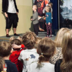 Na zdjęciu widać dzieci oglądające przedstawienie teatralne oraz aktora pirata, który stoi na scenie z trójką wybranych przedszkolaków.