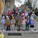 Na zdjęciu widać dzieci z grupy MISIAKÓW, dzieci stoją przed przedszkolem, trzymając w rękach papierowe kwiaty. Jest to zdjęcie grupowe.